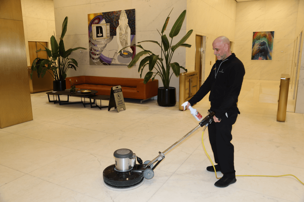 Man uses floor cleaner and spray in a high-end lobby space.